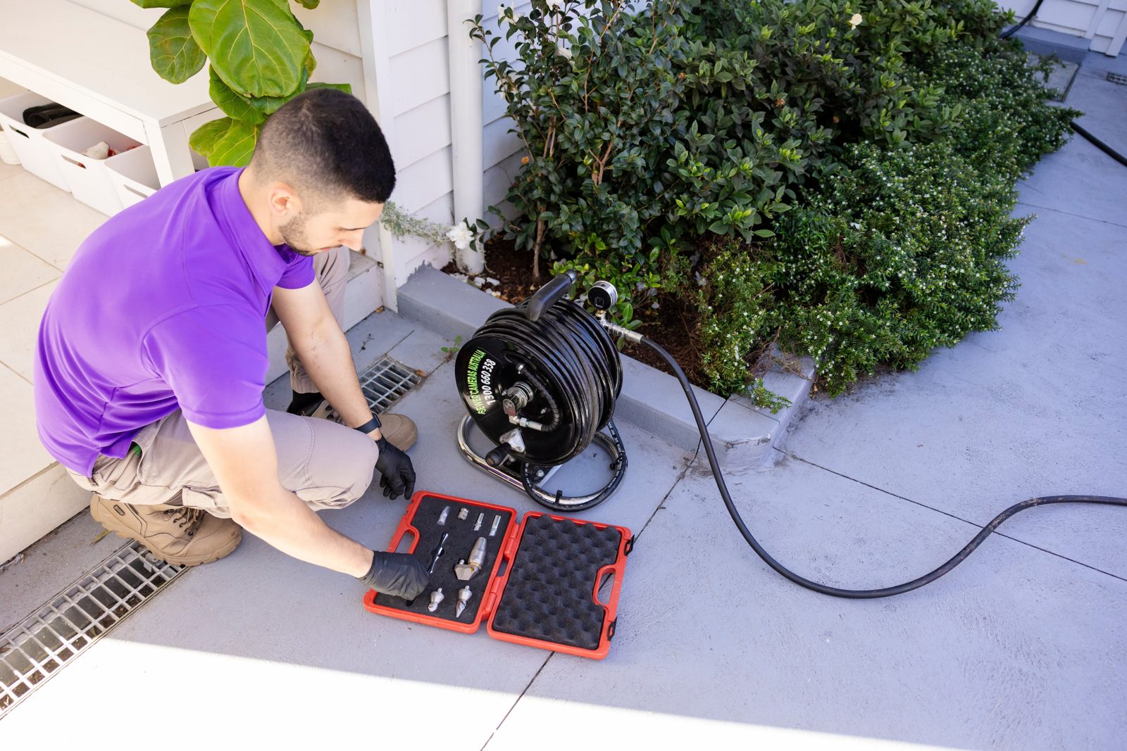 Miracle Plumbing plumber in a purple polo setting up high-pressure drain jetter nozzles beside a stormwater grate